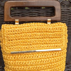Pode incluir: Uma bolsa de m&atilde;o de croch&ecirc; amarela com uma al&ccedil;a de madeira e um detalhe em metal dourado.