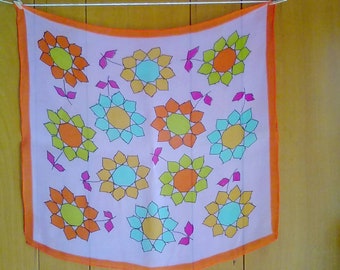 May include: A pink fabric scarf with an orange border and a pattern of colorful geometric flowers. The flowers are in shades of orange, yellow, green, and blue.