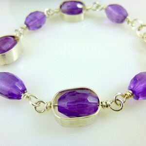 K&ouml;nnte beinhalten: Ein silbernes Kettenarmband mit violetten Amethyst-Edelsteinen. Das Armband hat einen Verschluss.