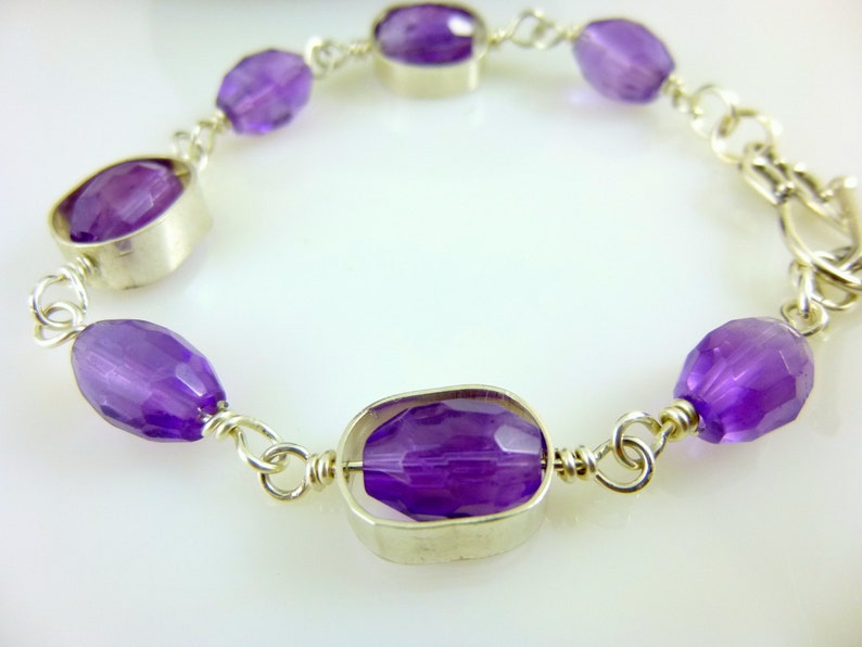 K&ouml;nnte beinhalten: Ein silbernes Kettenarmband mit violetten Amethyst-Edelsteinen. Das Armband hat einen Verschluss.