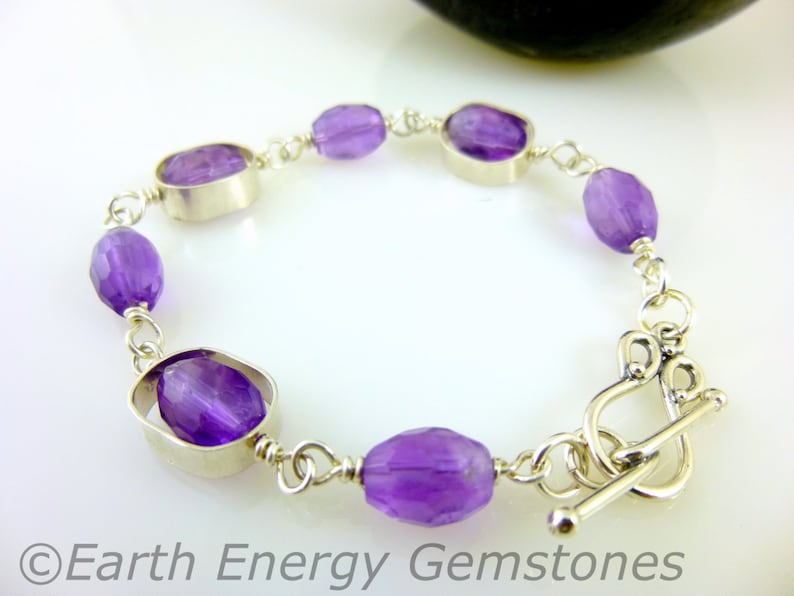 K&ouml;nnte beinhalten: Ein silbernes Armband mit einem Schiebeverschluss zeigt ovale Amethyst-Edelsteine, die in Silber gefasst sind.