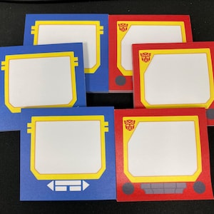 May include: Six square sticky notes in blue and red. Each note has a white center, a yellow border, and a design resembling a retro electronic device. Some notes feature a Transformers logo.