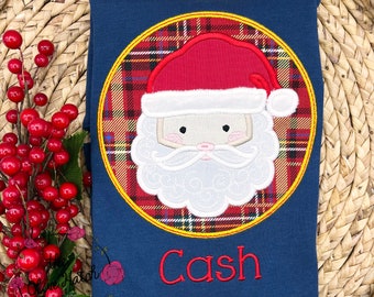 May include: Navy blue long-sleeve shirt with a Santa Claus applique. The Santa Claus design is inside a gold circle with a red and brown plaid background. The name "Cash" is embroidered in red below the Santa Claus design.