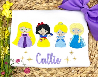 May include: White t-shirt with embroidered images of Disney princesses, including Snow White, Rapunzel, Cinderella, and Elsa. The shirt has the name "Callie" embroidered in purple below the princesses.