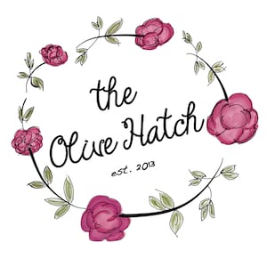 May include: A black and white logo with the text "the Olive Hatch est. 2013" surrounded by a wreath of pink flowers and green leaves.