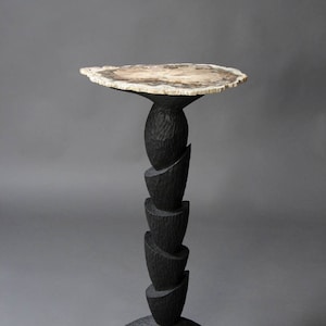 May include: A black wooden side table with a unique, layered base and a round, natural wood top.
