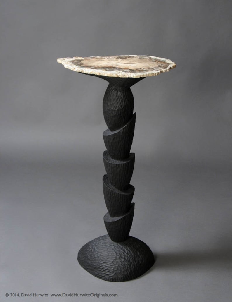May include: A black wooden side table with a unique, layered base and a round, natural wood top.