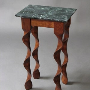 May include: A small, dark wood end table with a green marble top. The table has four legs that are twisted and turned.