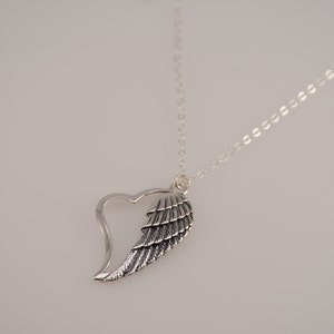 May include: A silver necklace with a heart-shaped pendant featuring a detailed angel wing design.