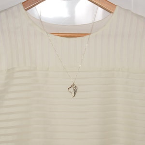 May include: A white sheer blouse with a silver necklace featuring a wing pendant.
