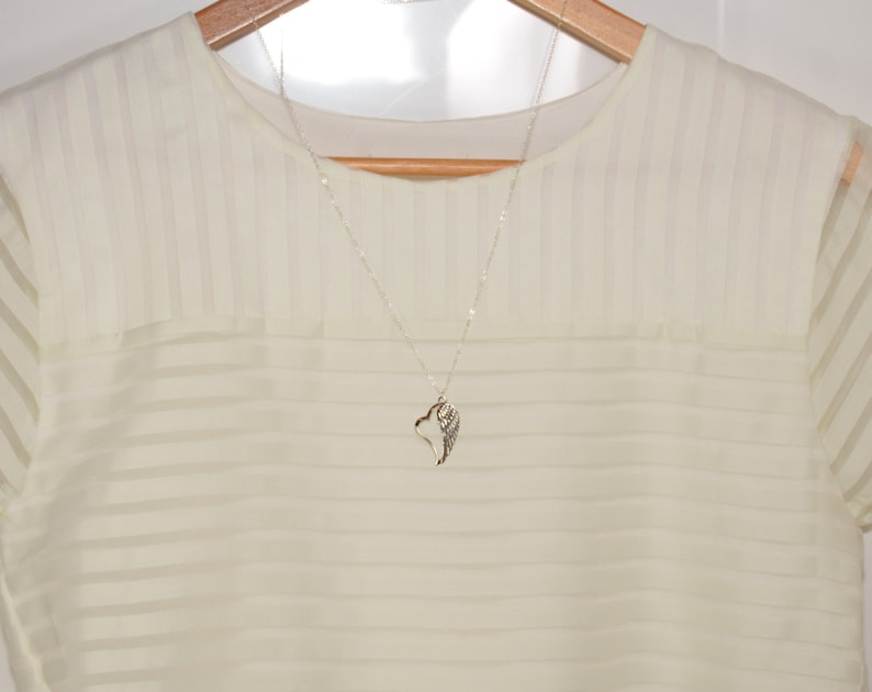 May include: A white sheer blouse with a silver necklace featuring a wing pendant.