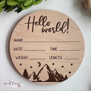 May include: A round wooden sign with the text "Hello World!" and spaces for a baby's name, date, time, weight, and length. The sign is decorated with a mountain range, a crescent moon, and stars.