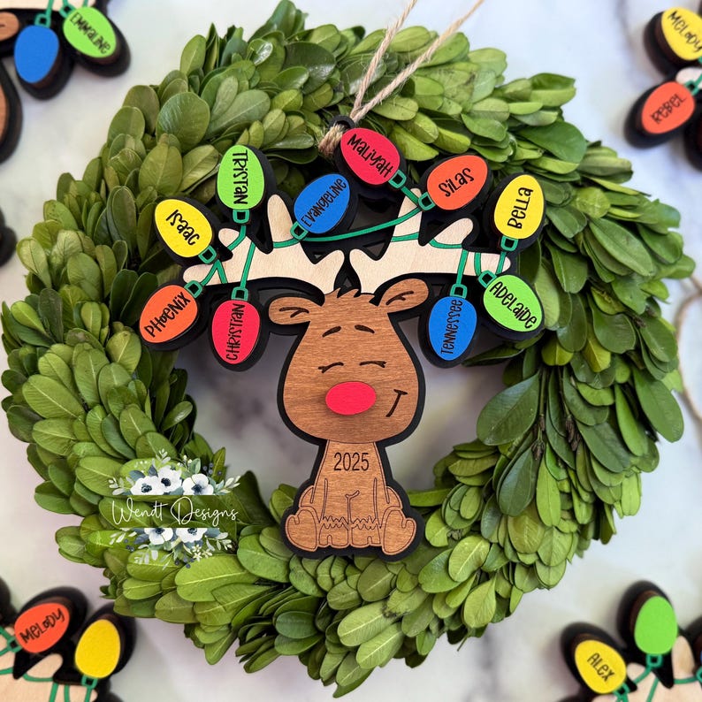 May include: A wooden reindeer ornament featuring a red nose and the year 2025, with antlers decorated by a string of colourful light bulb-shaped tags. Each tag is inscribed with a name, including Tristan, Isaac, Phoenix, Christian, Maliyah, Evangeline, Silas, Bella, Tennessee, and Adelaide.