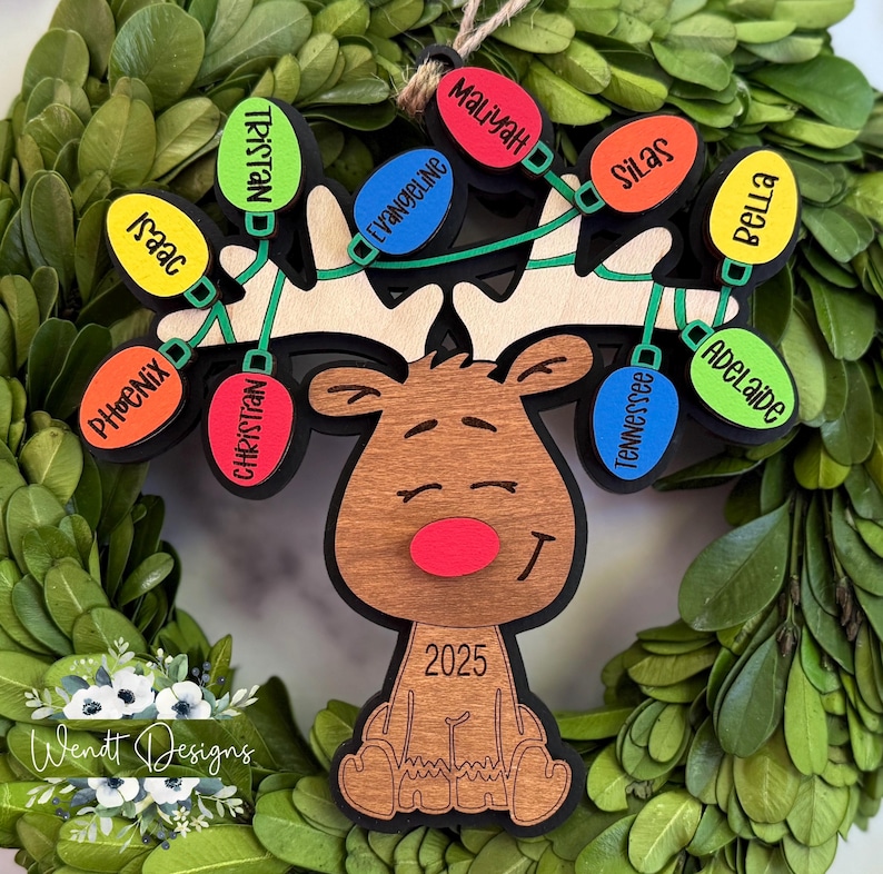 May include: A wooden reindeer ornament featuring a red nose and the year 2025. The antlers are decorated with a string of colourful light bulb shapes, each engraved with the names Tristan, Isaac, Phoenix, Christian, Evangeline, Maliyah, Silas, Tennessee, Bella, and Adelaide.
