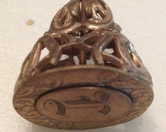 May include: A gold-toned metal seal with intricate designs and a raised circular area with a decorative pattern.