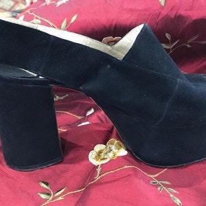 May include: Black suede platform sandals with a thick, block heel. The sandals have a slingback strap and an open toe.