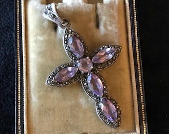 May include: A silver-toned cross pendant with amethyst-colored gemstones and marcasite accents. The cross is in a velvet-lined jewelry box. The gemstones are oval and round, set in a floral pattern.