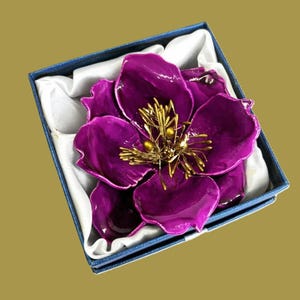 May include: A purple flower brooch with gold accents in a blue velvet box.
