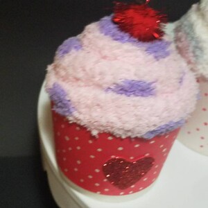 May include: A pink and purple cupcake with a red glitter heart on the front. The cupcake has a red glitter cherry on top.