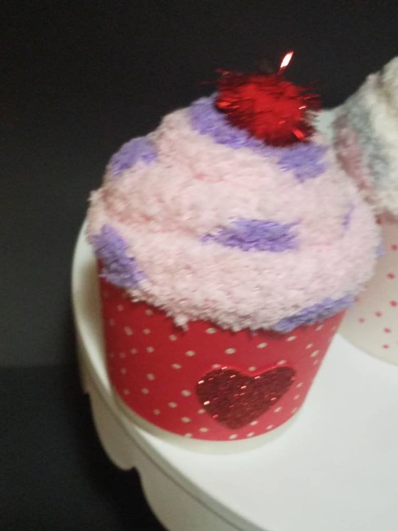 May include: A pink and purple cupcake with a red glitter heart on the front. The cupcake has a red glitter cherry on top.