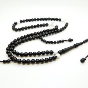 Peut inclure: Un chapelet noir avec des perles blanches parsemées. Les perles sont rondes et enfilées ensemble. Le chapelet a un gland marron foncé et une perle noire allongée à l'extrémité.