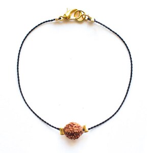May include: A black cord bracelet with a gold clasp and a brown seed bead charm.