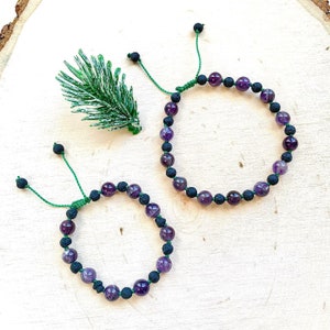 May include: Two bracelets with purple amethyst and black lava rock beads. The bracelets have green adjustable cords.