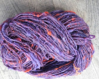 May include: A skein of yarn in shades of purple and orange. The yarn is hand-spun and has a rustic, textured look.