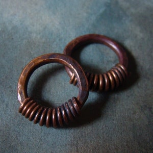 Könnte beinhalten: Zwei Kupferringe mit einem gewickelten Design. Die Ringe sind aus dickem Draht gefertigt und haben ein rustikales, gealtertes Aussehen.