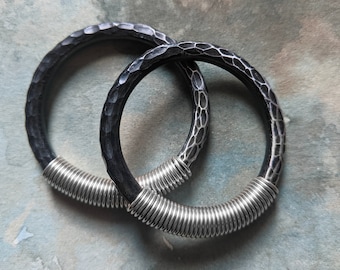 May include: Two black metal bracelets with a hammered texture and silver coiled wire accents.