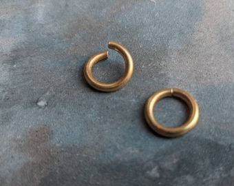 May include: Two gold jump rings, one slightly larger than the other, on a gray textured surface.