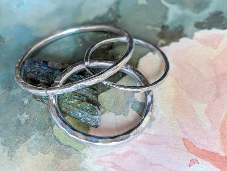 May include: Three silver hammered rings stacked on top of each other. The rings are smooth and shiny, and they have a slightly textured surface.