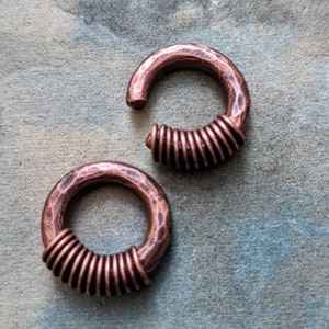 Puede incluir: Dos pendientes de aro de cobre con acabado martillado y dise&ntilde;o de alambre en espiral. Los pendientes son de color cobre c&aacute;lido y tienen un aspecto r&uacute;stico.