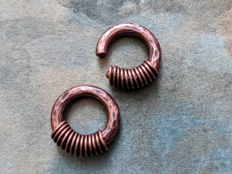 Puede incluir: Dos pendientes de aro de cobre con acabado martillado y dise&ntilde;o de alambre en espiral. Los pendientes son de color cobre c&aacute;lido y tienen un aspecto r&uacute;stico.