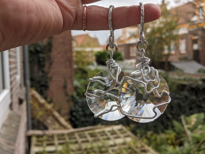 May include: A pair of silver-toned earrings with large, faceted crystal pendants. The crystals are round and held in place by a wire design. The earrings have hammered metal hooks.