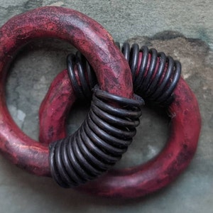 Puede incluir: Dos anillos de madera roja con una bobina de alambre negro envuelta alrededor de uno de los anillos. Los anillos est&aacute;n entrelazados.
