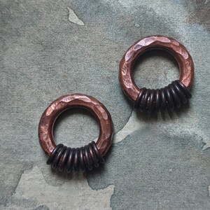 Puede incluir: Dos anillos de cobre martillados con alambre negro envuelto alrededor. Los anillos est&aacute;n sobre un fondo gris texturizado.