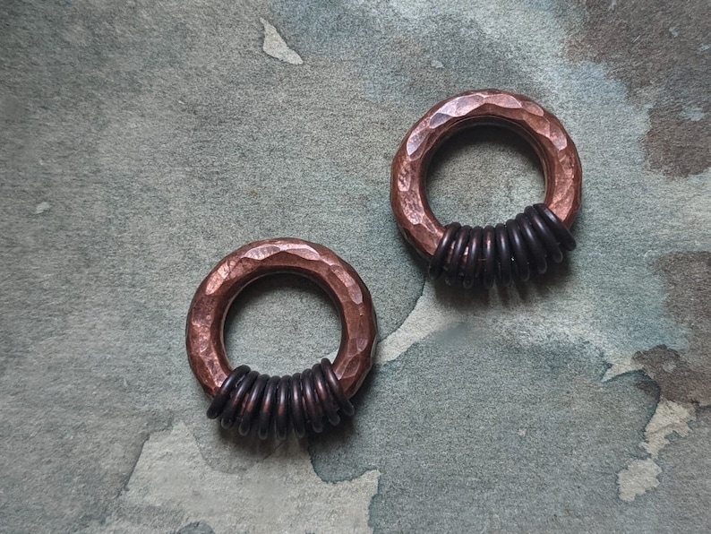 Puede incluir: Dos anillos de cobre martillados con alambre negro envuelto alrededor. Los anillos est&aacute;n sobre un fondo gris texturizado.