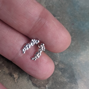 Op de afbeelding: Een paar zilverkleurige oorcrawlers, elk met een gebogen ontwerp bestaande uit kleine, bolvormige kralen. De oorbellen worden getoond tegen een neutrale achtergrond, wat hun delicate, getextureerde uiterlijk benadrukt. Een stijlvol accessoire.