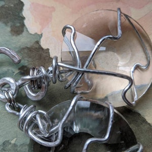 May include: A handmade bracelet featuring two large, clear, oval-shaped stones encased in a silver-colored wire. The wire is intricately wrapped around the stones and connected with a hook clasp.