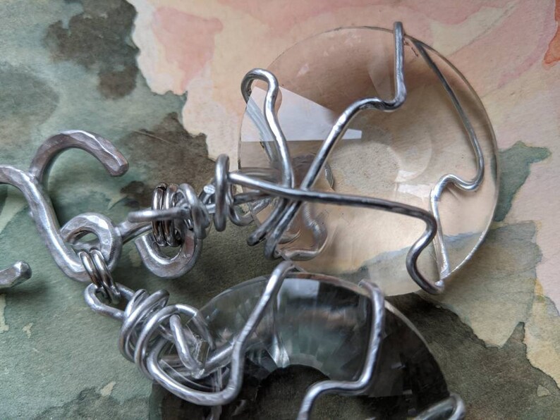 May include: A handmade bracelet featuring two large, clear, oval-shaped stones encased in a silver-colored wire. The wire is intricately wrapped around the stones and connected with a hook clasp.