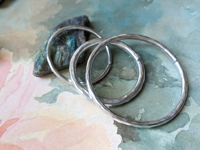 May include: Four silver hoop earrings with a hammered texture. The earrings are stacked on top of each other.
