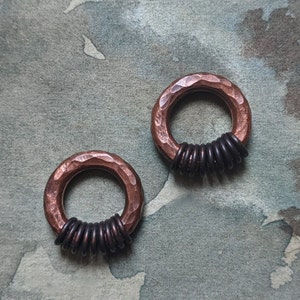 May include: Two copper rings with a hammered finish, each with a band of black metal rings around the center.