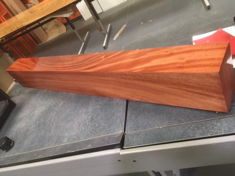 May include: A long, rectangular piece of polished wood with a reddish-brown color and a grain pattern. The wood is smooth and shiny.