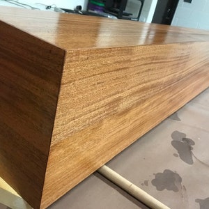 May include: A long, rectangular wooden shelf with a smooth, polished finish. The shelf is made of light brown wood with a natural grain pattern.