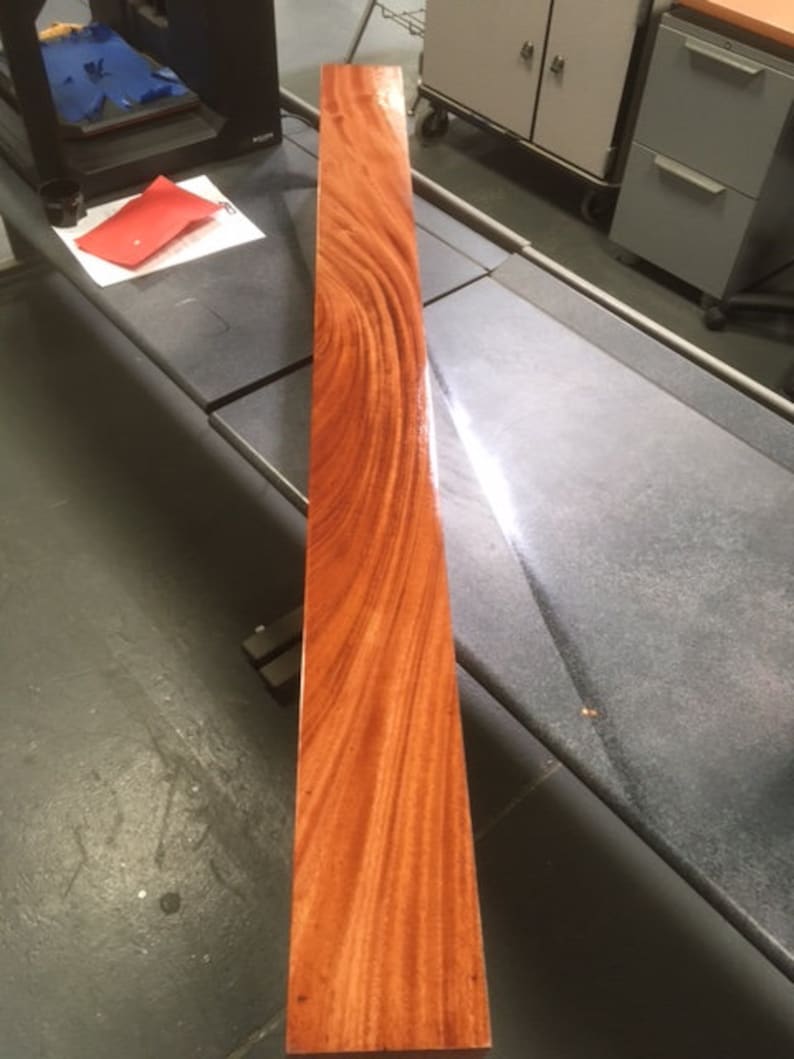May include: A long, narrow piece of wood with a rich reddish-brown color and a beautiful grain pattern. The wood has been polished to a high sheen.