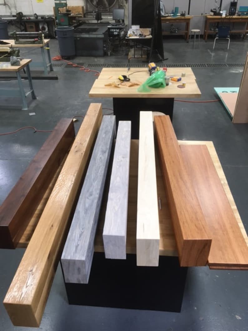 May include: Six wooden beams of different wood types and finishes. The beams are arranged in a row from left to right, with the darkest wood on the left and the lightest wood on the right. The beams are all about 12 inches long and 4 inches wide.