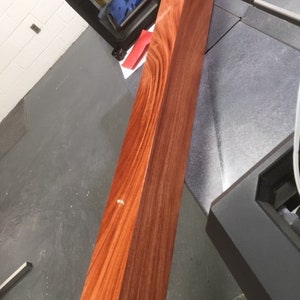 May include: A large, rectangular block of wood with a rich reddish-brown color. The wood grain is visible and has a beautiful pattern.