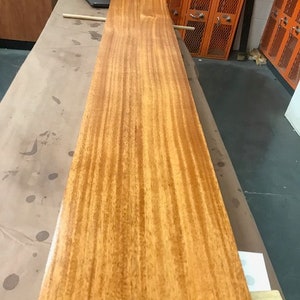 May include: A long, narrow piece of wood with a rich, reddish-brown color. The wood has a beautiful grain pattern and is smooth to the touch.