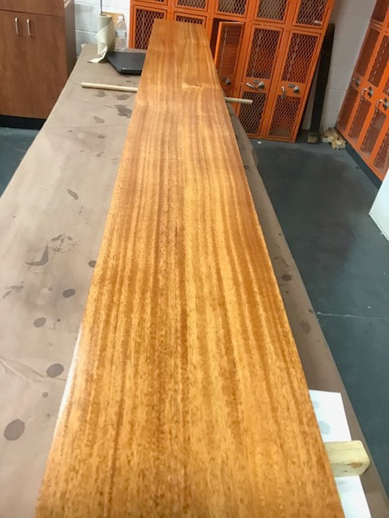 May include: A long, narrow piece of wood with a rich, reddish-brown color. The wood has a beautiful grain pattern and is smooth to the touch.